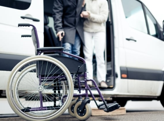 wheelchair in the foreground. Two people getting out of a van in the background